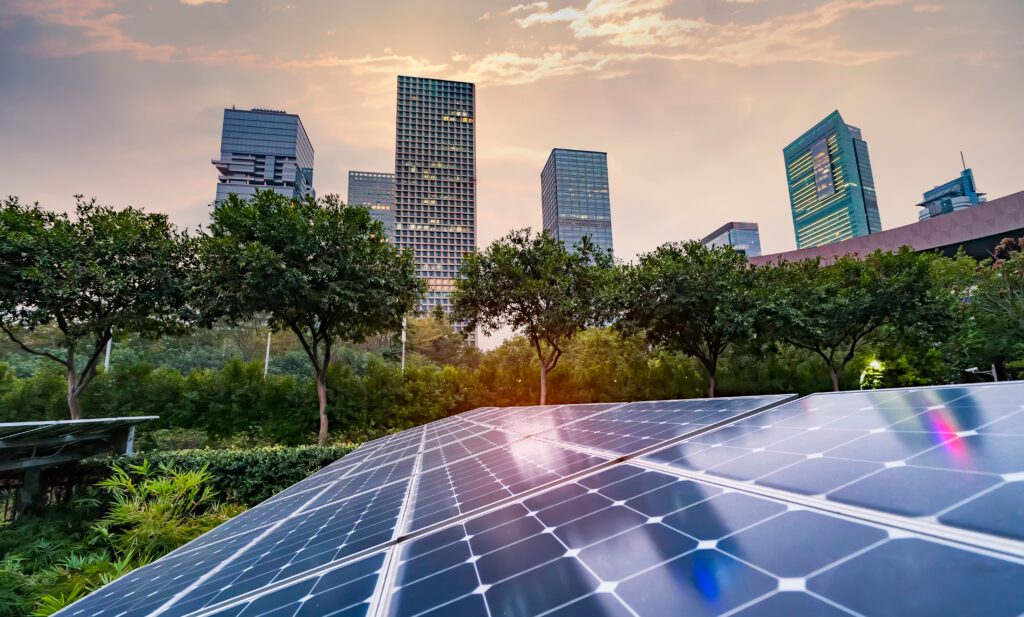 Painéis solares instalados em área verde com prédios comerciais ao fundo, representando a adoção de energia limpa em centros urbanos e a integração entre sustentabilidade e arquitetura moderna.