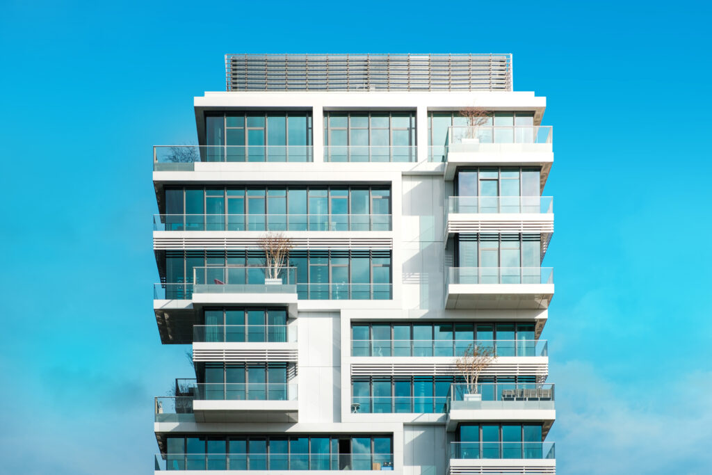 Prédio residencial moderno com varandas de vidro e fachada envidraçada, ideal para projetos de energia solar em condomínios verticalizados. Céu azul ao fundo realça o design contemporâneo do edifício.