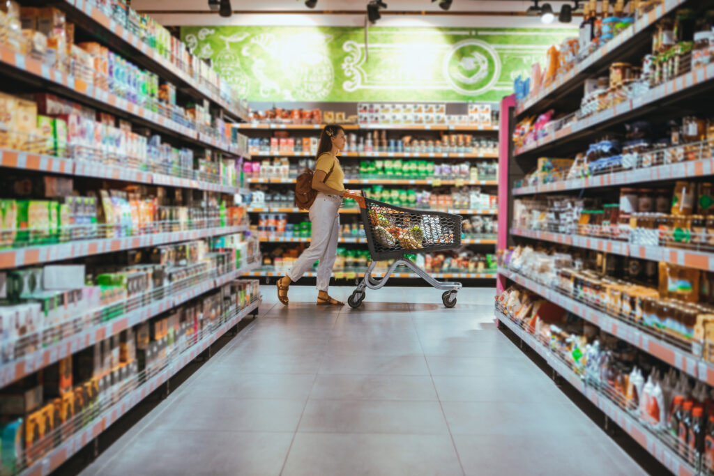 Colaboradora de supermercado usando tablet diante de refrigeradores, simbolizando eficiência e controle de consumo de energia.