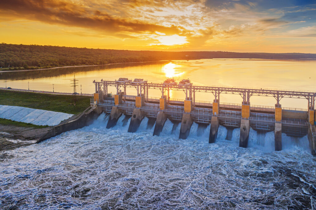 Hidrelétrica em operação ao entardecer, ilustrando os fatores climáticos que influenciam a geração de energia e afetam diretamente quem busca economizar na conta de luz.