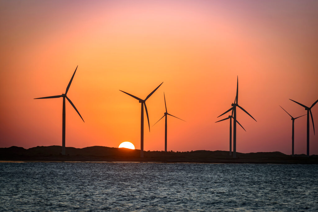 Parque eólico brasileiro ao entardecer, com turbinas de energia renovável à beira-mar. A imagem simboliza o protagonismo do Brasil na transição energética global e o uso crescente de inteligência artificial para otimizar a geração e distribuição de energia limpa.